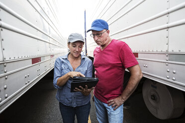 Kaukasischer Mann und Frau, die als Lkw-Fahrerteam auf einem Rastplatz zwischen den Lkw stehen und Daten auf einem Handy durchgehen. - MINF07905