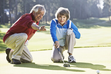 Ein älteres Paar diskutiert auf dem Grün eines Golfplatzes über die Richtung des Putts. - MINF07925