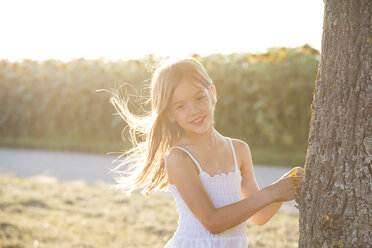 Girl standing on tree trunk at summer evening - LVF07389