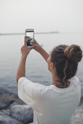 Teenage girl taking pictures of the sea with her smartphone - ACPF00202