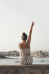 Teenage girl wearing striped beach wear, sitting on wall with raised arm - ACPF00212