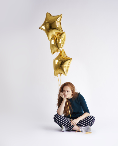 Porträt einer jungen Frau mit drei goldenen sternförmigen Luftballons, lizenzfreies Stockfoto