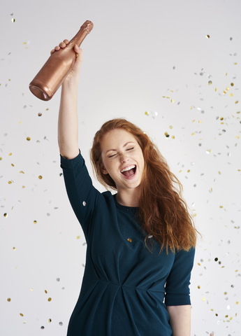 Porträt einer glücklichen jungen Frau mit einer Flasche Champagner bei einem Konfettiregen, lizenzfreies Stockfoto