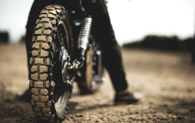 Rückansicht eines Mannes auf einem Cafe-Racer-Motorrad auf einem staubigen Feldweg, Nahaufnahme eines Reifens. - MINF07953