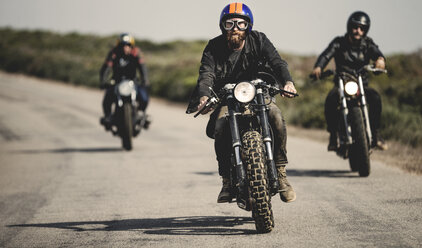 Drei Männer mit offenen Sturzhelmen und Schutzbrillen fahren mit Cafe-Racer-Motorrädern eine Landstraße entlang. - MINF07959