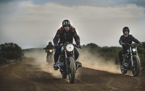 Drei Männer auf Cafe-Racer-Motorrädern auf einem staubigen Feldweg., lizenzfreies Stockfoto