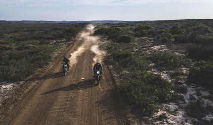 Landschaft mit zwei Männern, die auf einem staubigen Feldweg Cafe Racer-Motorräder im Kreis fahren. - MINF07970