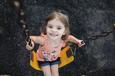 High angle view of smiling young girl sitting on swing, looking at camera. - MINF07984