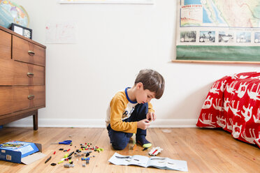 Junge mit braunem Haar, der in einem Kinderzimmer auf dem Hartholzboden kniet und mit Bauklötzen spielt. - MINF07988