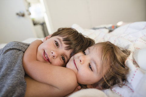 Lächelnder Junge mit braunem Haar und junges Mädchen liegen auf einem Bett und umarmen sich., lizenzfreies Stockfoto