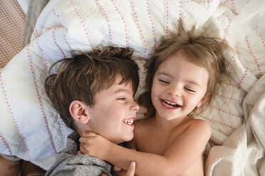 High angle view of smiling boy with brown hair and young girl lying on a bed, hugging. - MINF08000