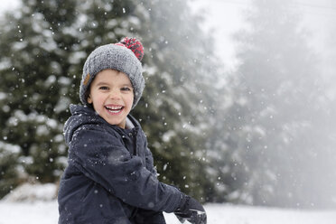 Lächelnder Junge mit grauer Strickmütze, der im Freien im Schnee steht und in die Kamera schaut. - MINF08002