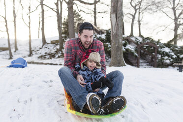 Ein lächelnder Mann und ein Junge mit Pelzmütze fahren auf einem Schlitten im Schnee einen Abhang hinunter. - MINF08009