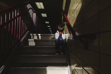 Boy with brown hair sitting in the shade on a staircase, head in hands. - MINF08014