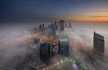 Luftaufnahme einer Stadtlandschaft mit beleuchteten Wolkenkratzern über den Wolken in Dubai, Vereinigte Arabische Emirate, in der Abenddämmerung. - MINF08047