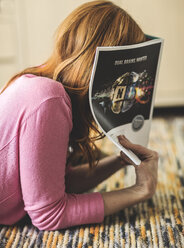 A woman lying on a rug and hiding her face in a magazine. - MINF08074