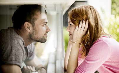 A couple smiling at each other through a pane of glass of a window. - MINF08077