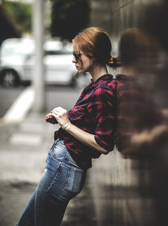 A woman leaning against a wall on a sidewalk. - MINF08093