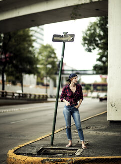 A woman standing at a road junction under a road bridge. - MINF08095