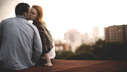 Ein Paar sitzt und küsst sich auf dem Dach einer Stadt. - MINF08104