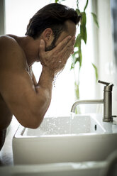 Ein Mann steht vor einem Waschbecken im Badezimmer und wäscht sich das Gesicht. - MINF08116