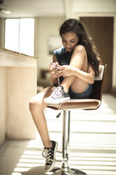 A girl sitting at a kitchen counter looking at a mobile phone screen. - MINF08121