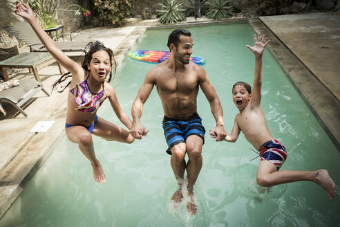 Ein Mann hält zwei Kinder an der Hand, die rückwärts in ein Schwimmbecken springen. - MINF08151