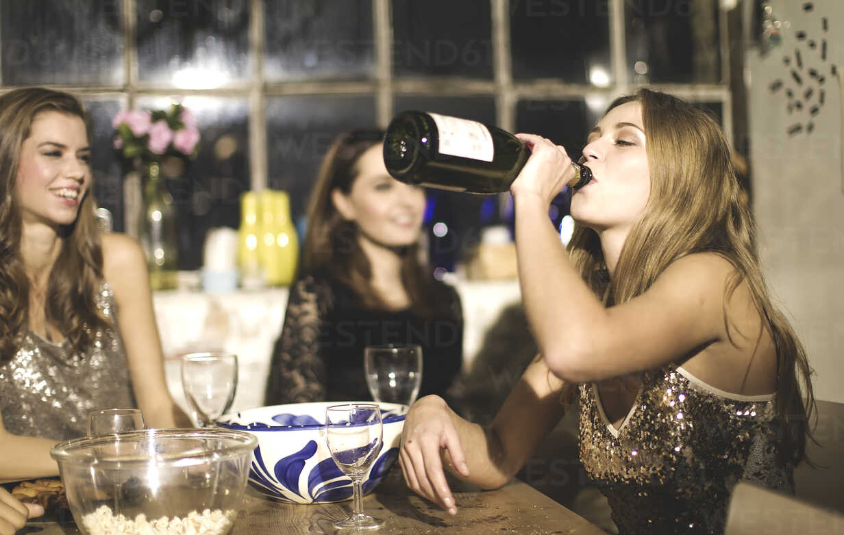A group of friends around a table at a party, one girl drinking from a  bottle of champagne. stock photo