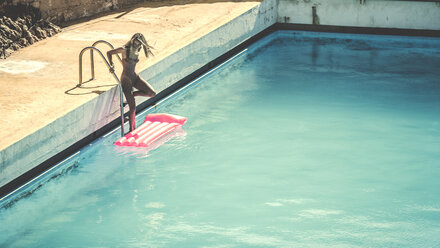 A young woman wearing a swimsuit climbing into a swimming pool with a pool raft. - MINF08189