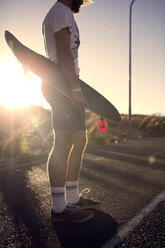 Ein junger Mann steht auf einer Straße und hält ein Skateboard. - MINF08195