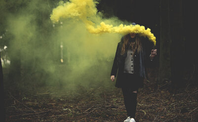 A young woman waving a yellow smoke flare in a forest. - MINF08198