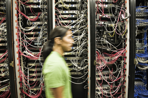 Asiatisch-amerikanischer männlicher Techniker bei der Arbeit an einem CAT-5-Kabelbündelungssystem in einem großen Computerserverraum., lizenzfreies Stockfoto