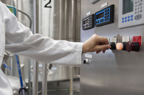 A technician in a white coat turns on the controls to processing tanks in a large bottling plant. - MINF08201