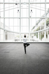 Businessman relaxing doing a yoga pose in a large open glass covered walkway. - MINF08205