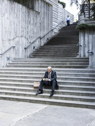 Schwarzer Geschäftsmann, der auf einer Treppenstufe sitzend eine Mittagspause macht. - MINF08207
