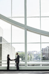Businessman and woman meeting in a large glass covered walkway - MINF08212