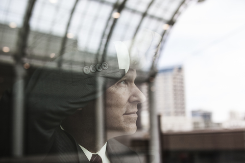 Kaukasischer Geschäftsmann, der aus einem Fenster mit Spiegelungen starrt., lizenzfreies Stockfoto