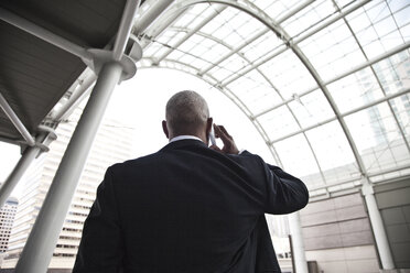 Black businessman on the phone while walking through a large glass covered walkway. - MINF08222