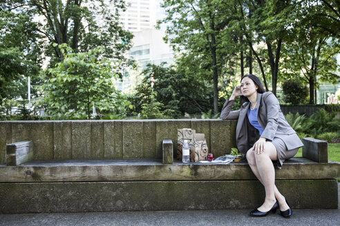 Eine Geschäftsfrau, die in einem Stadtpark auf einer Bank sitzend ihre Mittagspause macht. - MINF08226