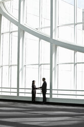 Businessman and woman meeting in a large glass covered walkway - MINF08230