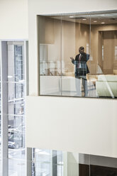 Black businessman on the phone standing in a conference room window. - MINF08244