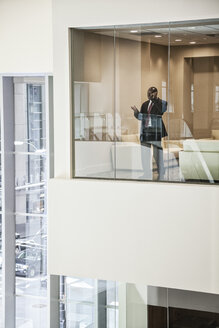 Schwarzer Geschäftsmann am Telefon, der am Fenster eines Konferenzraums steht. - MINF08244