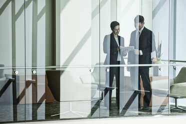 Businessman and woman standing behind a conference room window in large business centre. - MINF08250