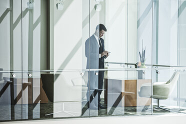 Businessman standing behind a conference room window in a large business centre. - MINF08251