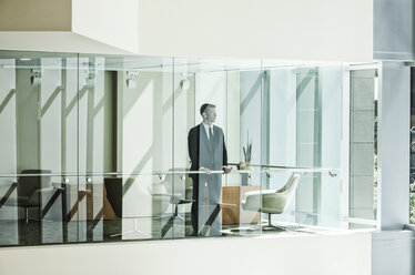 Geschäftsmann, der hinter dem Fenster eines Konferenzraums in einem großen Geschäftszentrum steht. - MINF08253