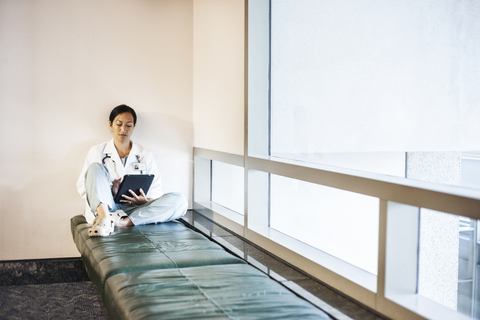 Asiatische Ärztin, die einen Notebook-Computer benutzt und einen Laborkittel und ein Stethoskop trägt., lizenzfreies Stockfoto