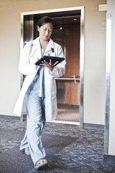 Asiatische Ärztin, die in einem Krankenhausflur spazieren geht, während sie an einem Notebook-Computer arbeitet. - MINF08269