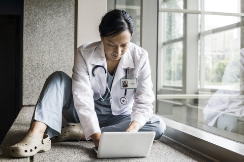 Asiatische Ärztin bei der Arbeit an einem Laptop in einem Krankenhausflur., lizenzfreies Stockfoto