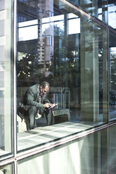 Ein schwarzer Geschäftsmann schreibt eine SMS, während er vor einer großen Witwe im Wartebereich einer Lobby sitzt. - MINF08278