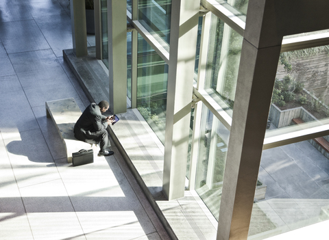 Schwarzer Geschäftsmann an einem Notebook in einem Wartebereich einer großen offenen Lobby., lizenzfreies Stockfoto